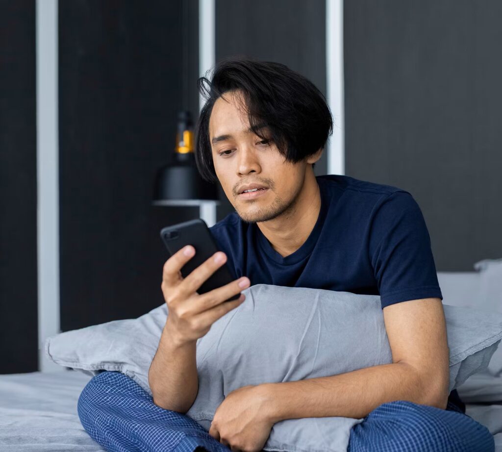 A man sitting on his bed looking at his mobile phone