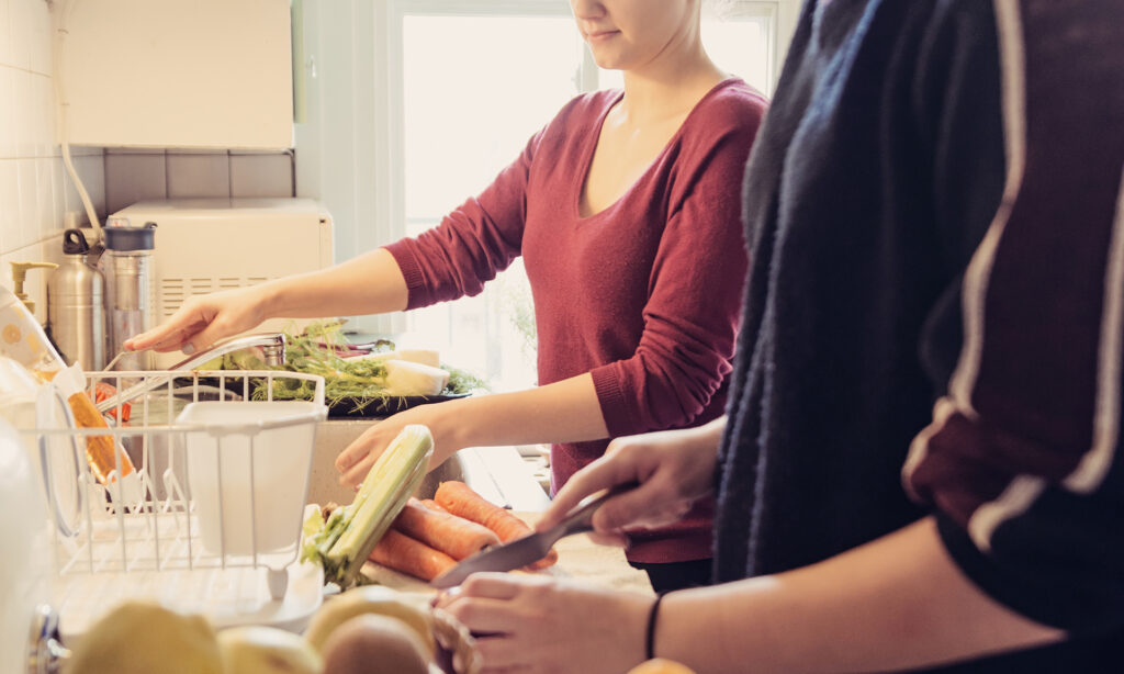 Two young woman preparing food on the bench of small kitchen.