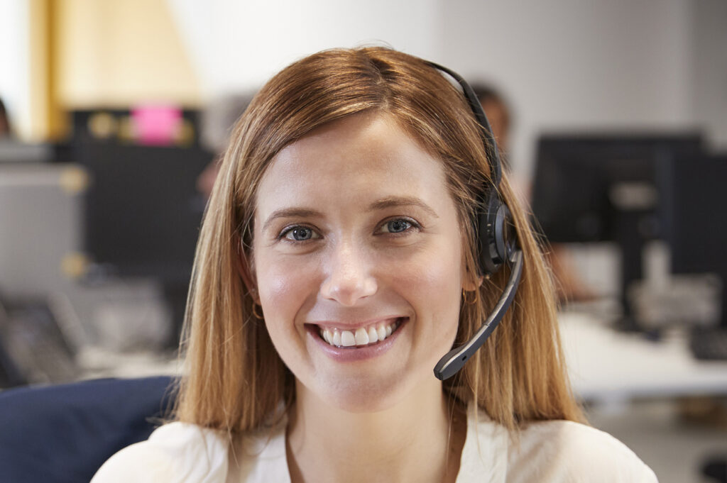 Young woman working at computer with headset in busy office