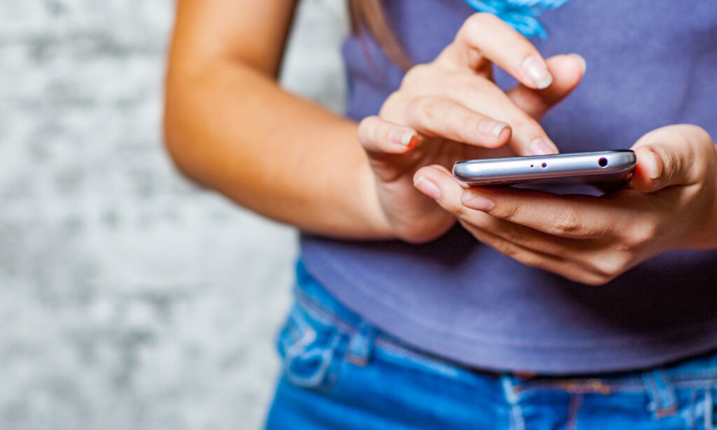 young teenag girls hands using mobile phone or smartphone on gray wall background