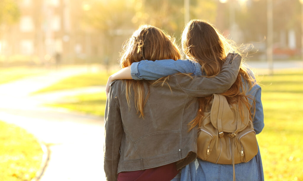 Affectionate friends with long hair walking at sunset in a park