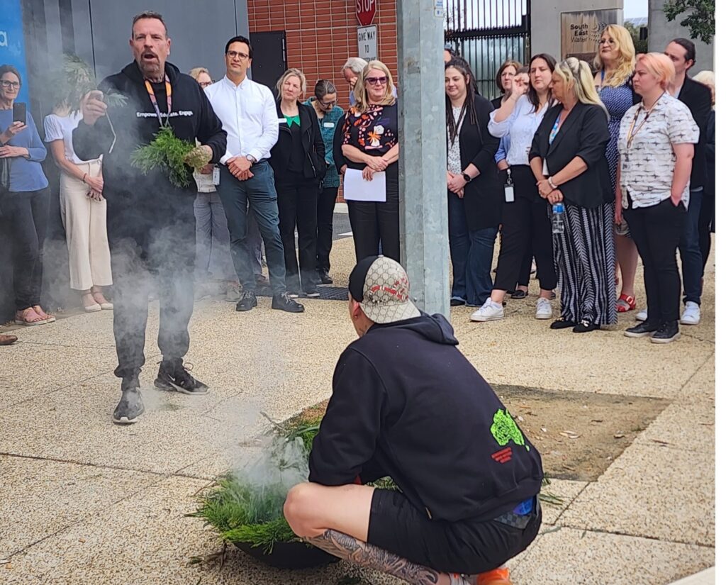 Indigenous men perform a smoking ceremony on the street outside the Frankston Local Services building