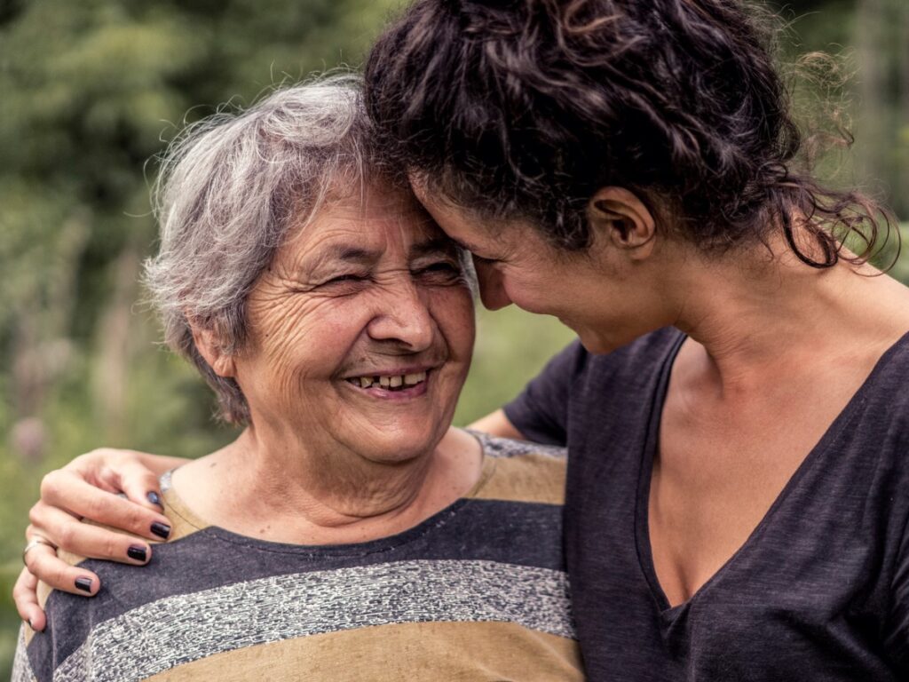 Woman with her arm around her elderly mother who is smiling.