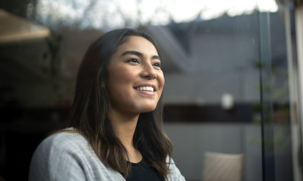 Happy young woman contemplating while looking out the window