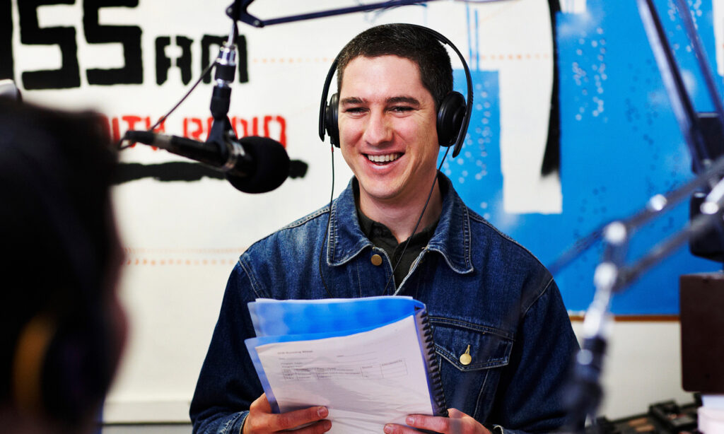 A man standing in a radio booth recording a podcast