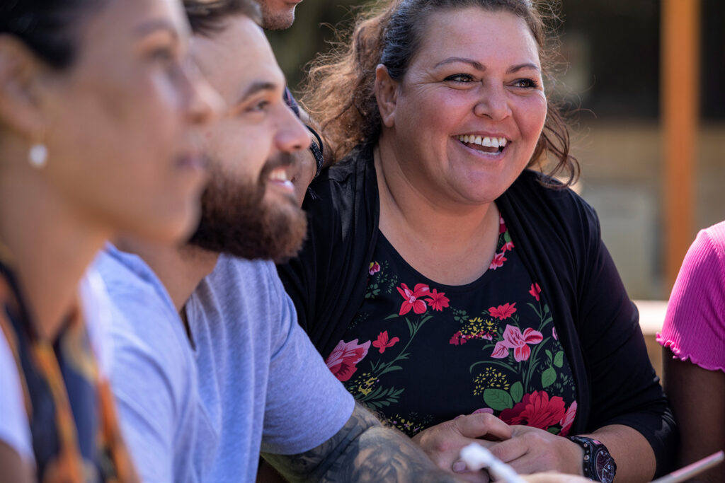 A group of people. A lady in the background smiling wearing a floral shirt.