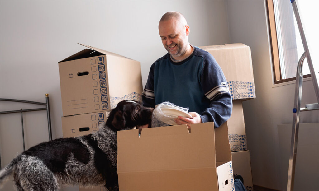 A man and his dog unpack boxes in a bedroom