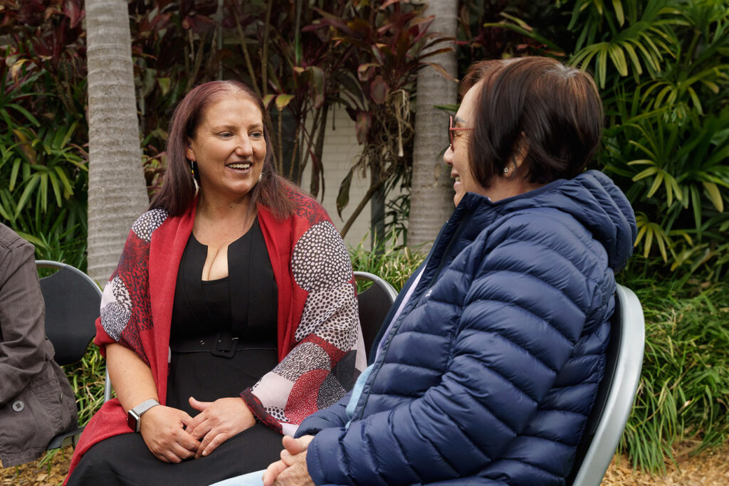 Two people sitting on chairs in a garden speaking happily.