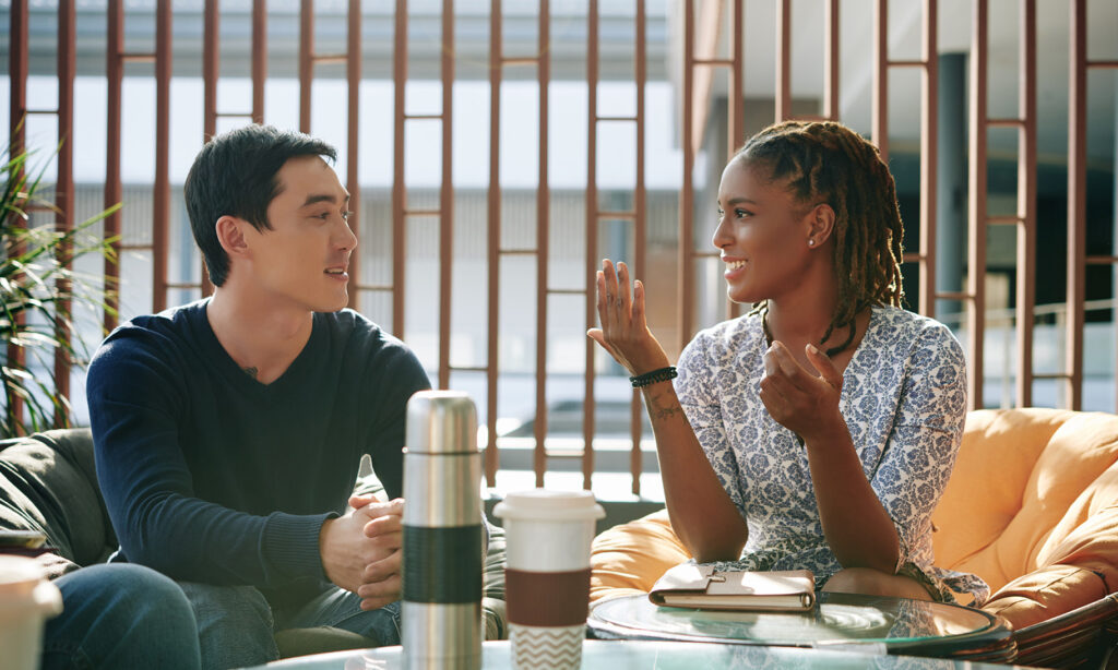 Positive emotional young businesswoman discussing news and ideas with colleague at meeting