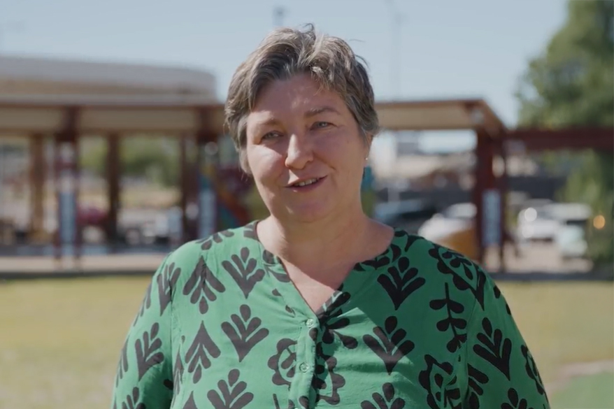 A lady standing in a park wearing a green patterned shirt.