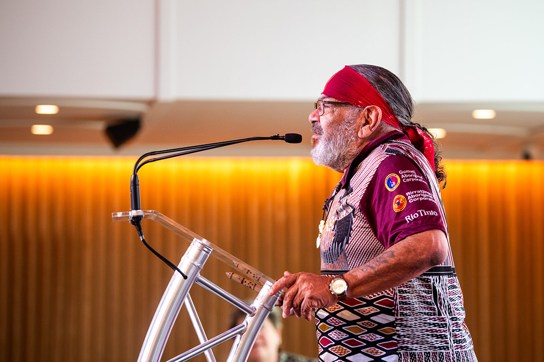 A person wearing a red bandana and maroon shirt speaks into a microphone.