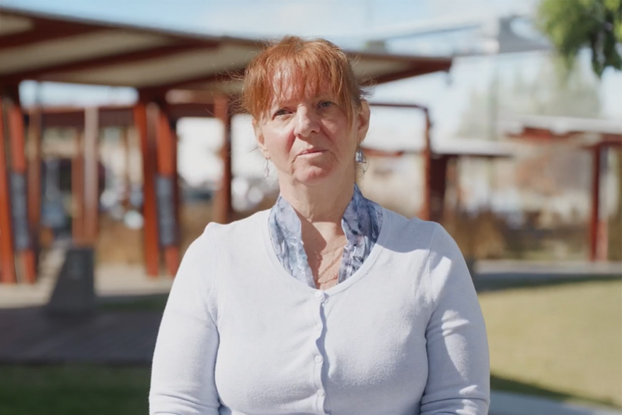 Woman standing in a park wearing a white cardigan.