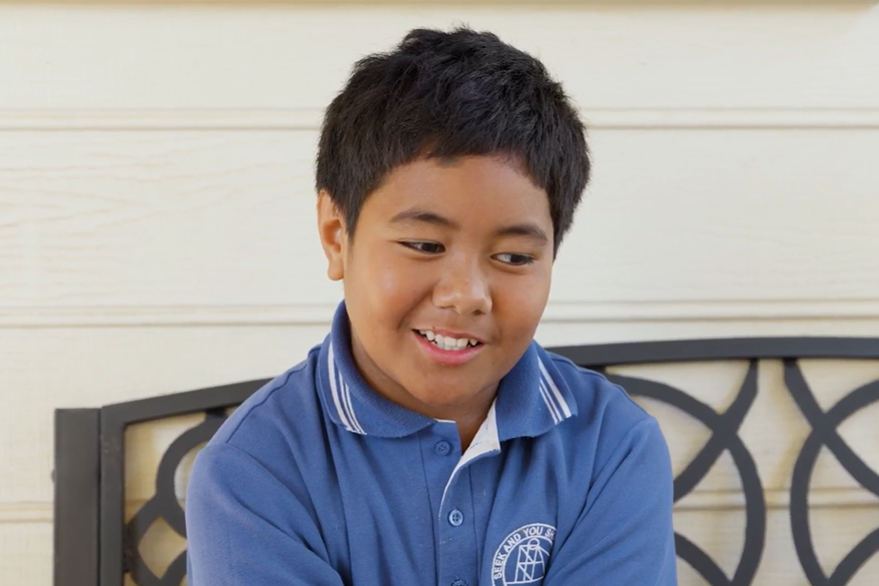 Little boy sitting on a bench in a blue shirt smiling.