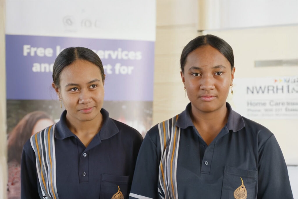 Two girls standing next to each other in dark blue school uniforms.