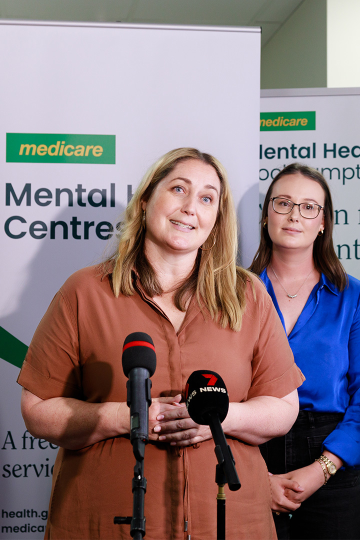 The Honorable Emma McBride MP speaks to the press in front of Medicare Mental Health Centre branded pull up banners. 