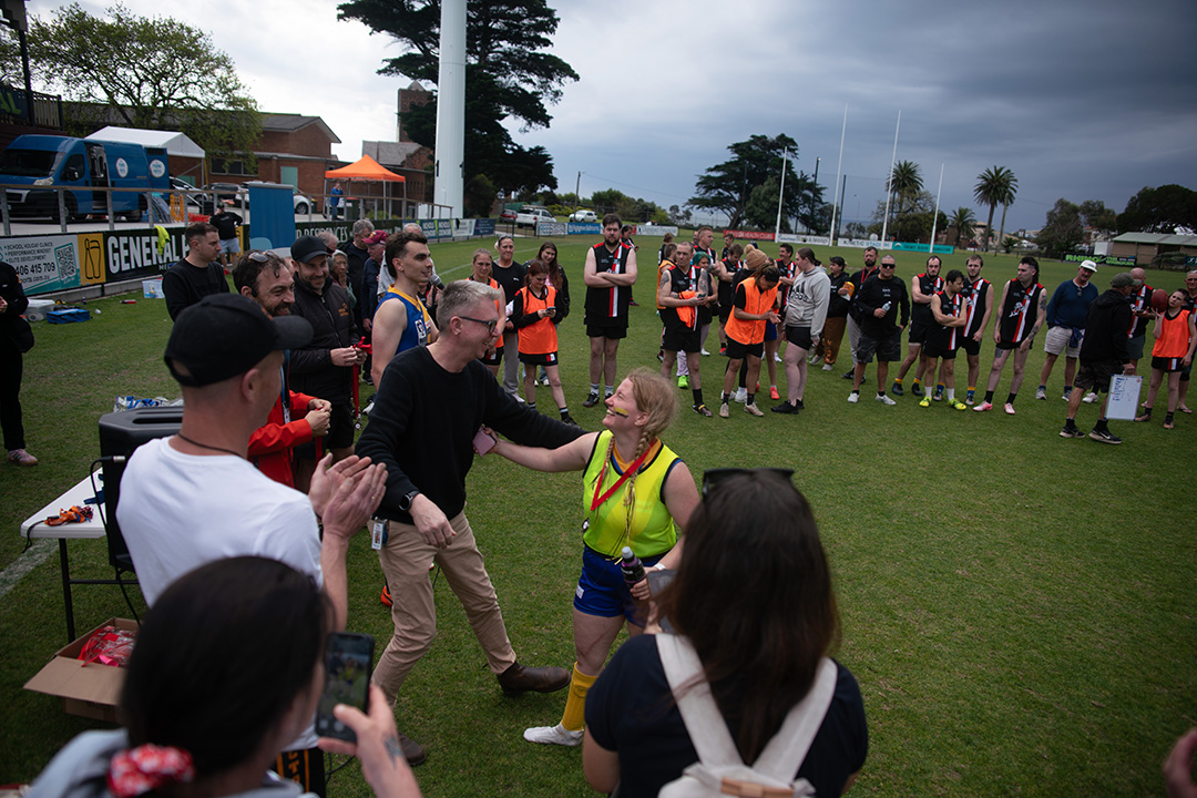 People on the field cheering and clapping as a man congratulates a woman