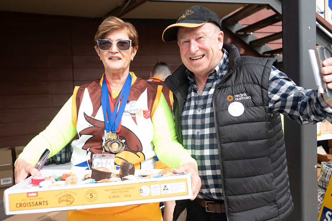 A lady holding a box of cupcakes and a man smiling