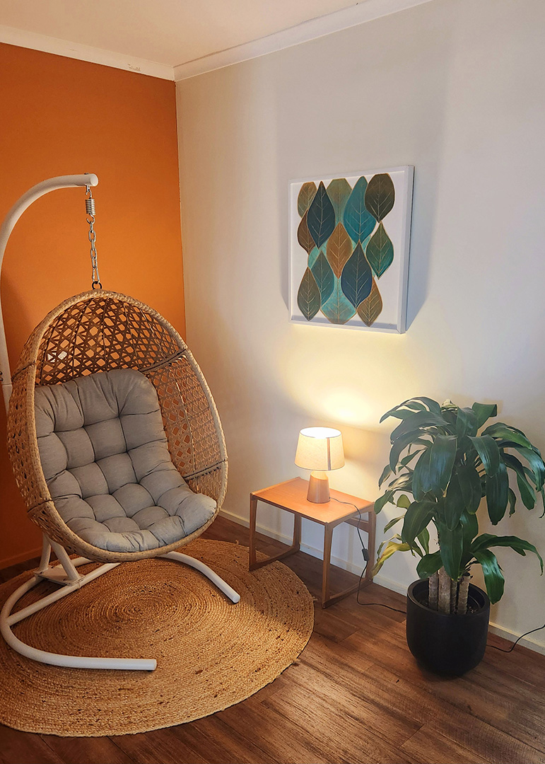 A warm lit room with an orange wall, a hanging chair and an indoor plant.