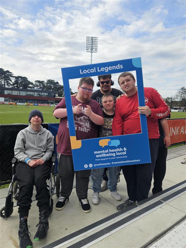 A group of football enthusiasts pose for a photo behind a blue frame. 