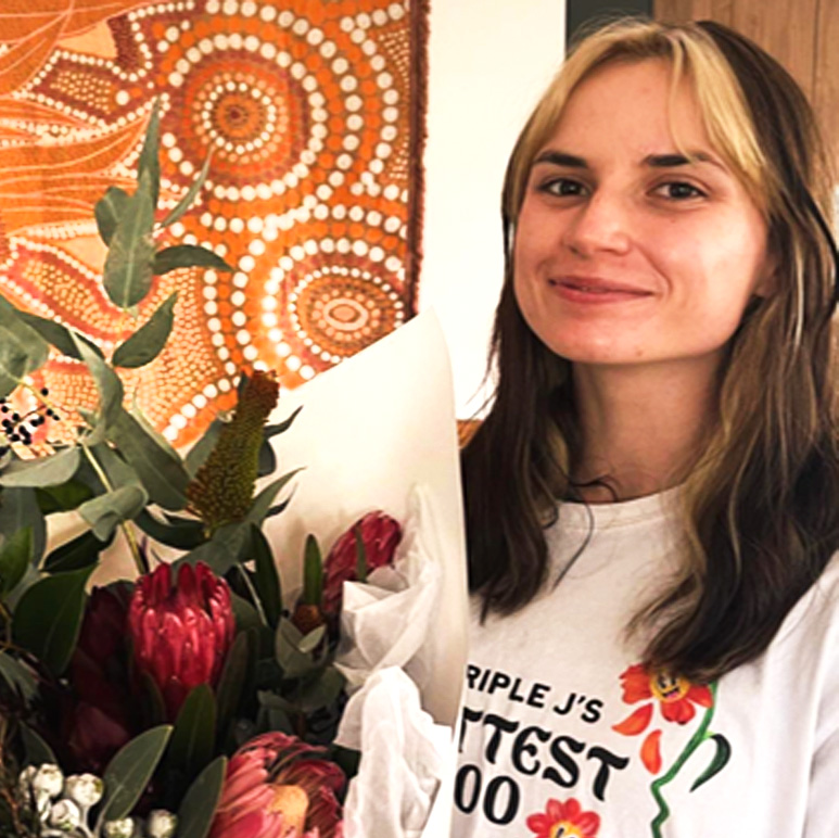 A person with brown hair holding a bouquet of flowers wearing a white t-shirt.