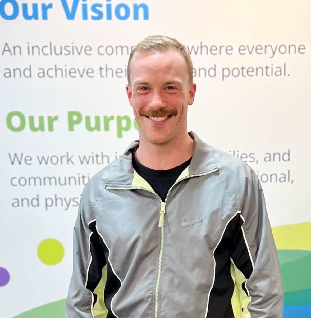 Person smiling at camera in front of a wall with Wellways signage.