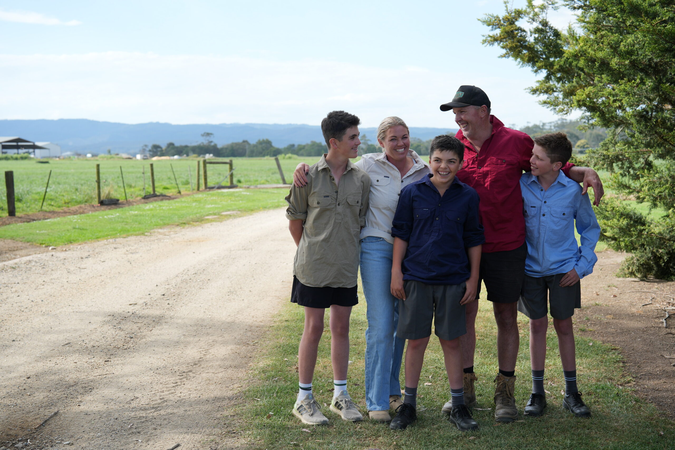 A group of people stand next to a dirt road laughing in the countryside.