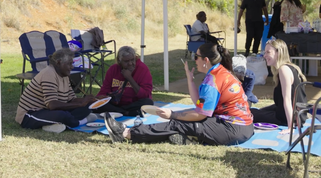 Group of people sitting on the ground doing indigenous painting